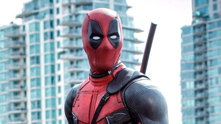 Deadpool standing in front of several tall buildings. 