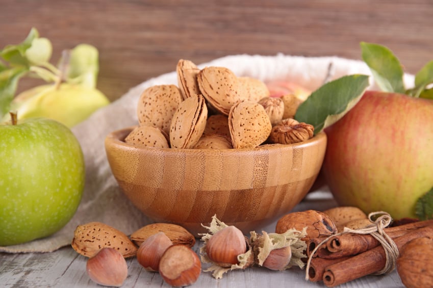 bowl of unshelled almonds with a red and reen apple