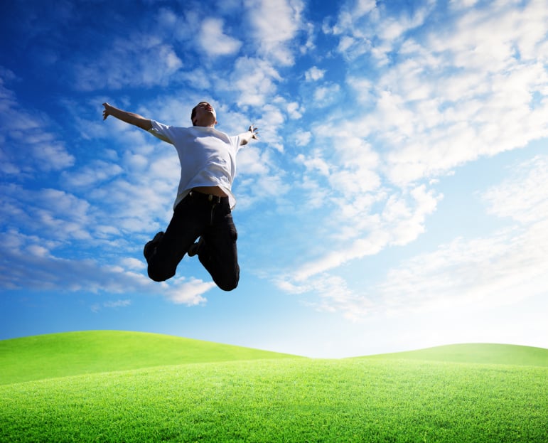 man jumping in a field with blue sky and clouds