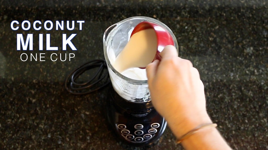 adding coconut milk to a blender with ice