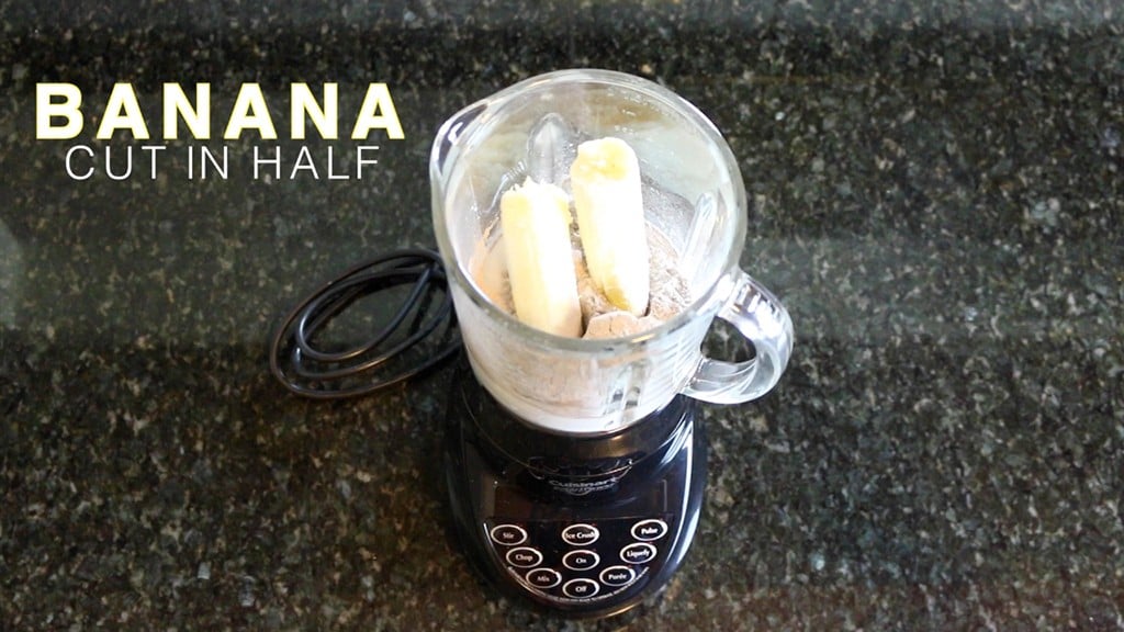adding a halved banana to a blender for a protein shake