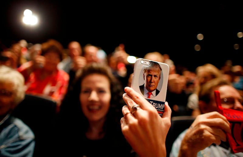a Donald Trump supporter holds a phone with Trump's face on it at a rally