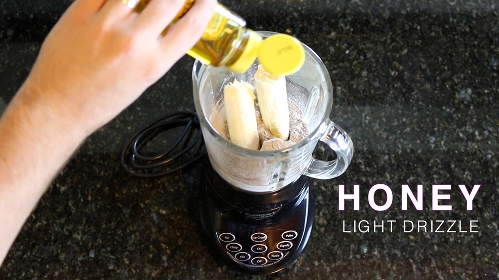 adding honey to a blender filled with ice, coconut milk, and a banana