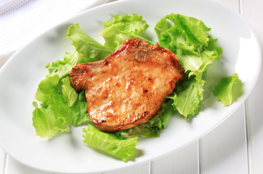 glazed pork chop on lettuce leaves over a white platter