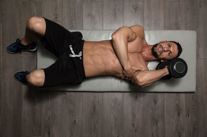 man lying on an exercise mat lifting a dumbbell with one hand man lying on an exercise mat lifting a dumbbell with one hand
