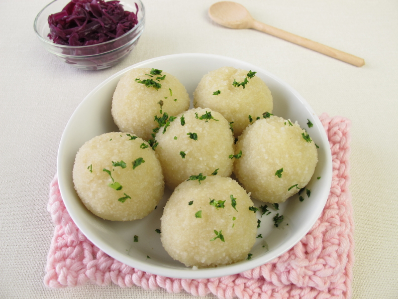 bowl of potato dumplings with parsley and a side of braised red cabbage