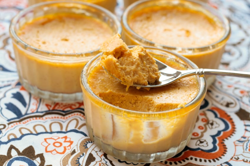 three glass bowls of pumpkin custard with a spoon