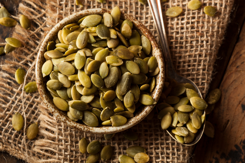 bowl of pumpkin seeds with a spoon over a burlap sack bowl of pumpkin seeds with a spoon over a burlap sack