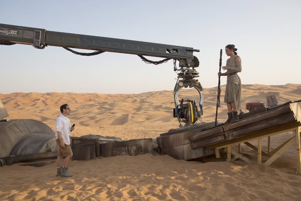 J.J. Abrams and Daisy Ridley standing on set in a dessert speaking