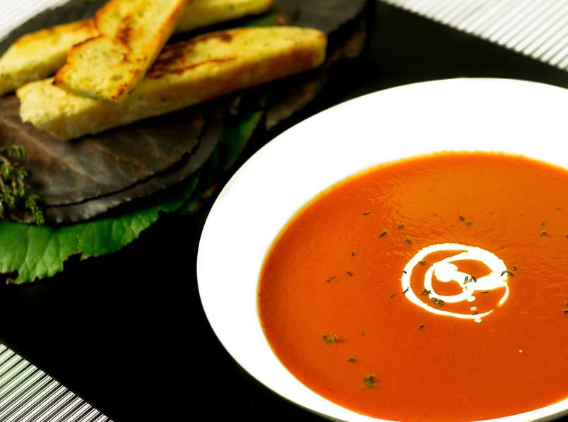 roasted red pepper and tomato soup in a white bowl with bread