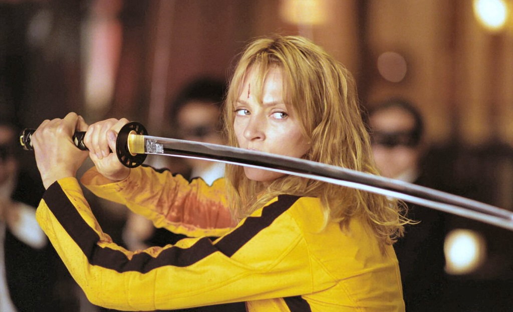 Uma Thurman in a yellow jumpsuit, holding a sword parallel to the ground across her shoulder