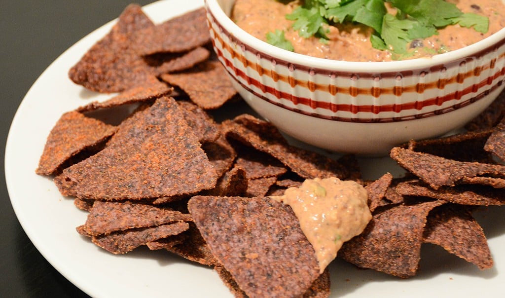 close up of a blue corn tortilla dipped into creamy black bean dip