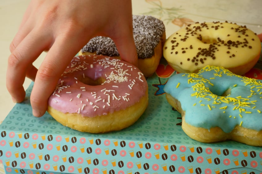 hand reaching for a doughnut with sprinkles and frosting from a variety box