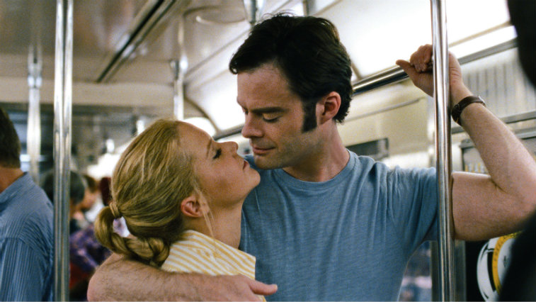 Bill Hader is holding onto a pole on the subway train and is about kiss Amy Schumer.
