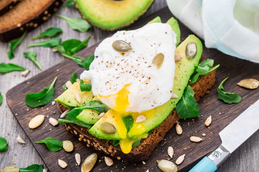 breakfast sandwich with a poached egg, sliced avocado, and greens on whole-grain bread