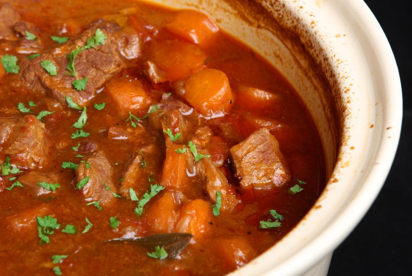 beef stew in a ceramic dish with tomatoes and carrots
