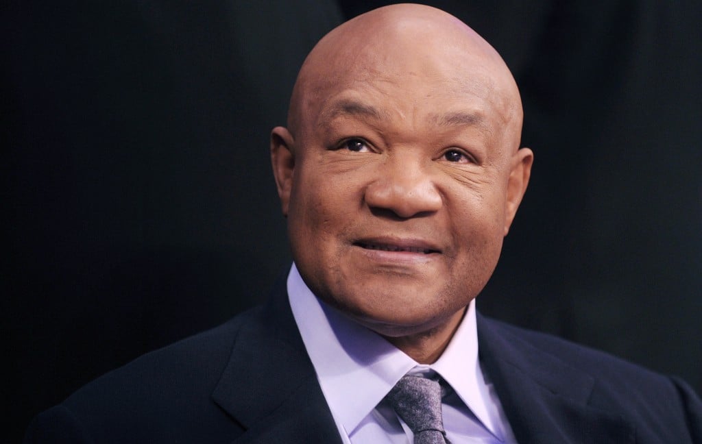 George Foreman is in a purple shirt and tie and dark jacket.