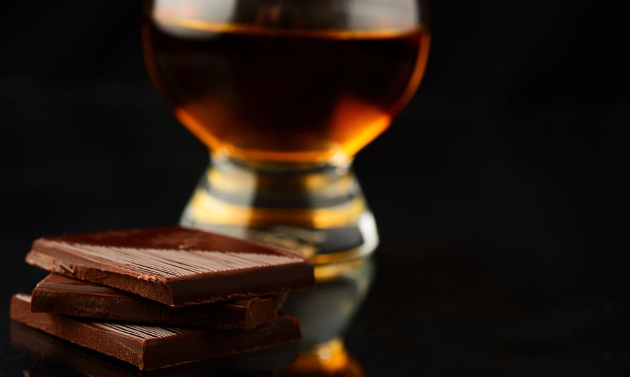 stack of dark chocolate with a glass of whiskey in the background