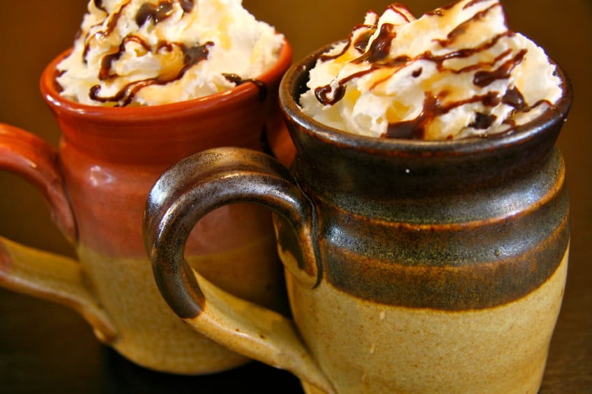two mugs of hot chocolate with whipped cream drizzled with caramel and chocolate