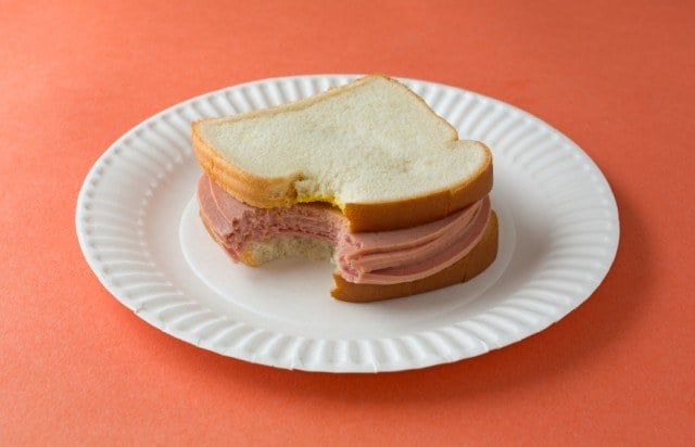 bologna sandwich with mustard on white bread that's been bitten