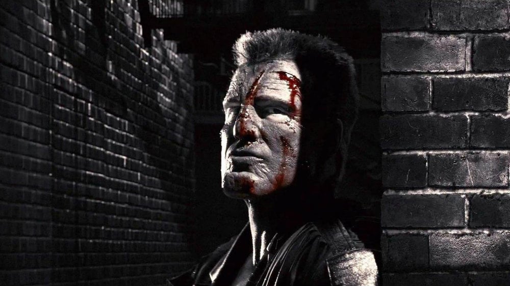 A bloodied Mickey Rourke in Sin City, cloaked in shadows and looking to his left