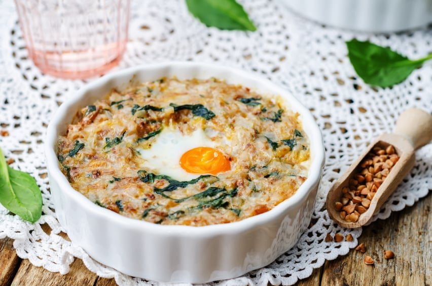 baked casserole with buckwheat, spinach, cheese, and an egg in a white ramekin