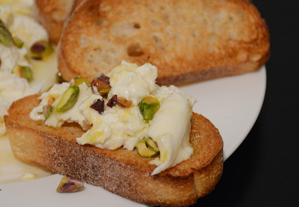 slice of toasted bread smeared with burrata and topped with dressing and pistachios