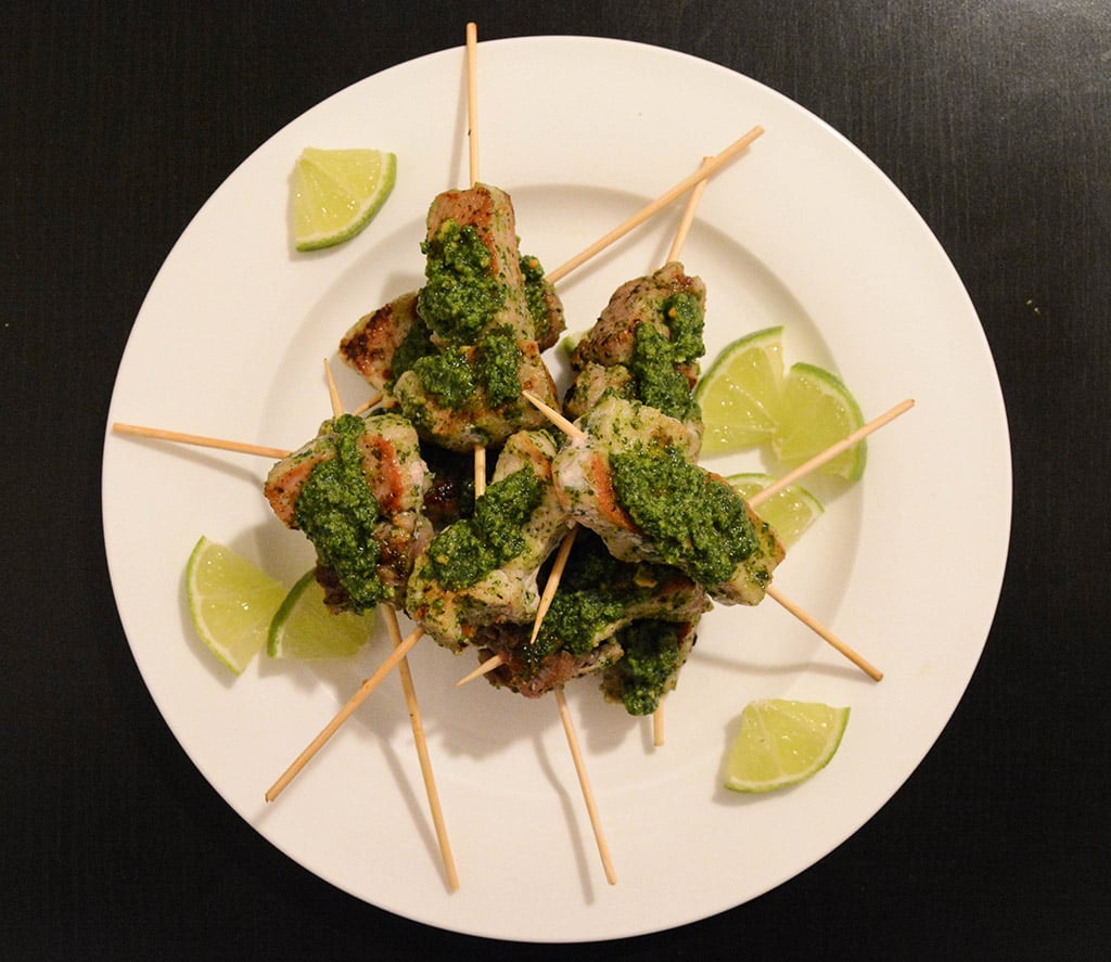 cilantro-peanut pork skewers on a white plate with lime wedges