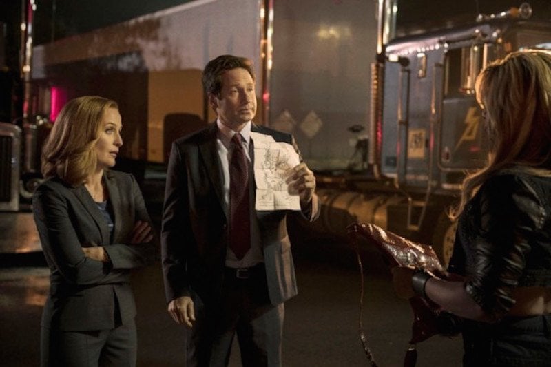 The cast of exfiles stands in a room in suits