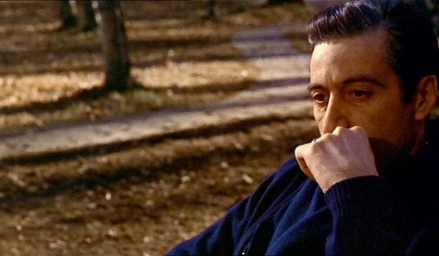 Al Pacino as Michael Corleone and sitting on a bench in The Godfather.
