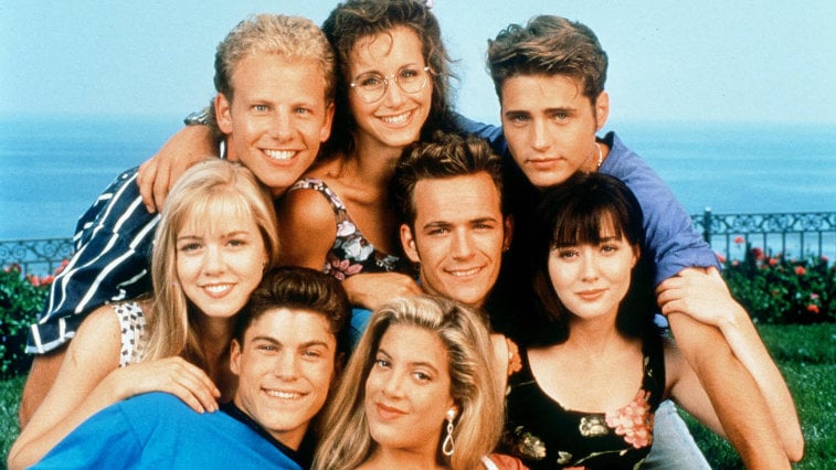 The cast of 'Beverly Hills, 90210' stands together in front of an ocean. The cast of 'Beverly Hills, 90210' stands together in front of an ocean.