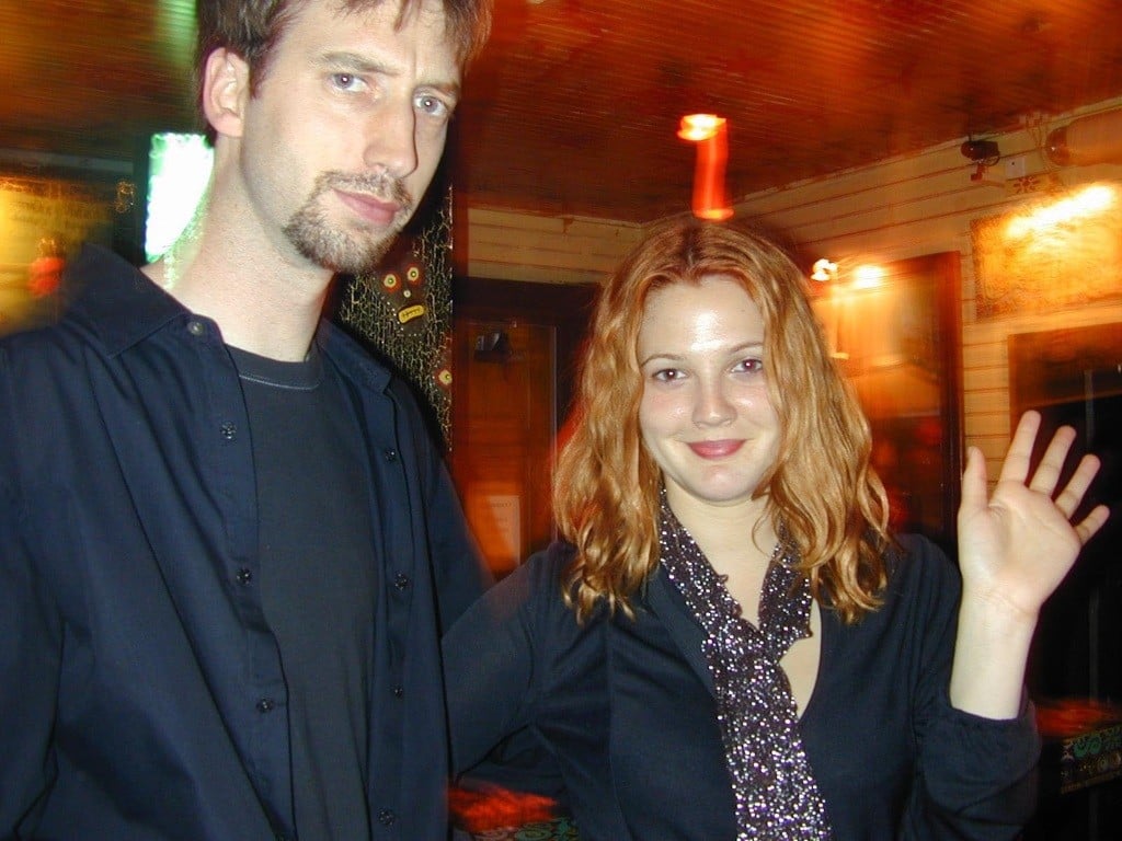 Drew Barrymore smiles and waves at the camera, while Tom Green looks on bemused