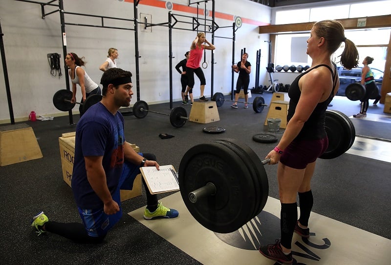 woman performs a deadlift while a trainer watches