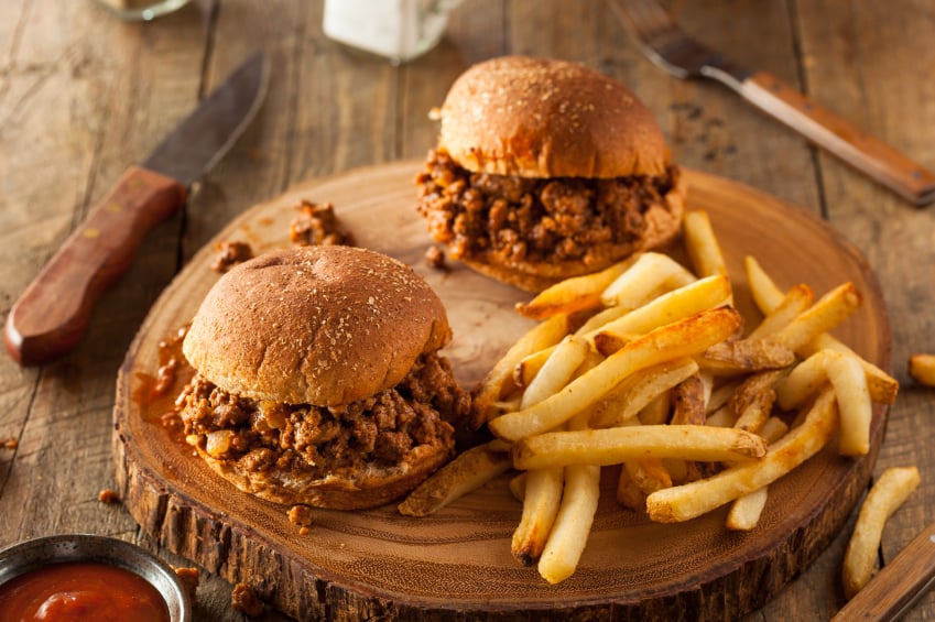 two sloppy joe sandwiches on buns with a pile of french fries