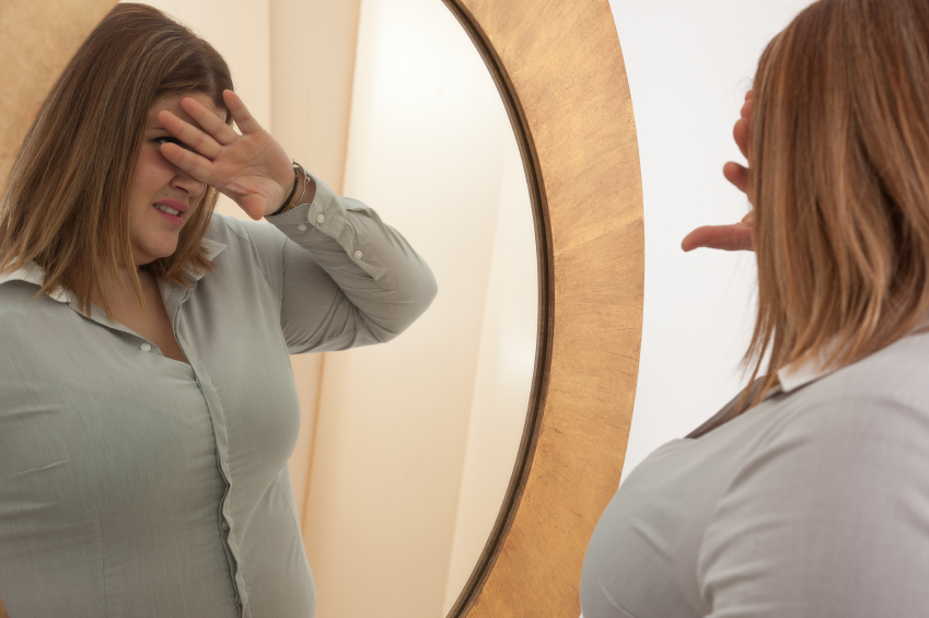 woman with bad body image or low self esteem looking in the mirror