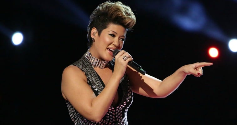 Tessanne Chin is singing and pointing to the left on The Voice.
