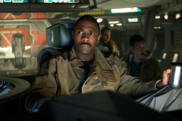 Idris Elba as Janek in a uniform in a commanding chair on a ship holding a cup in Prometheus