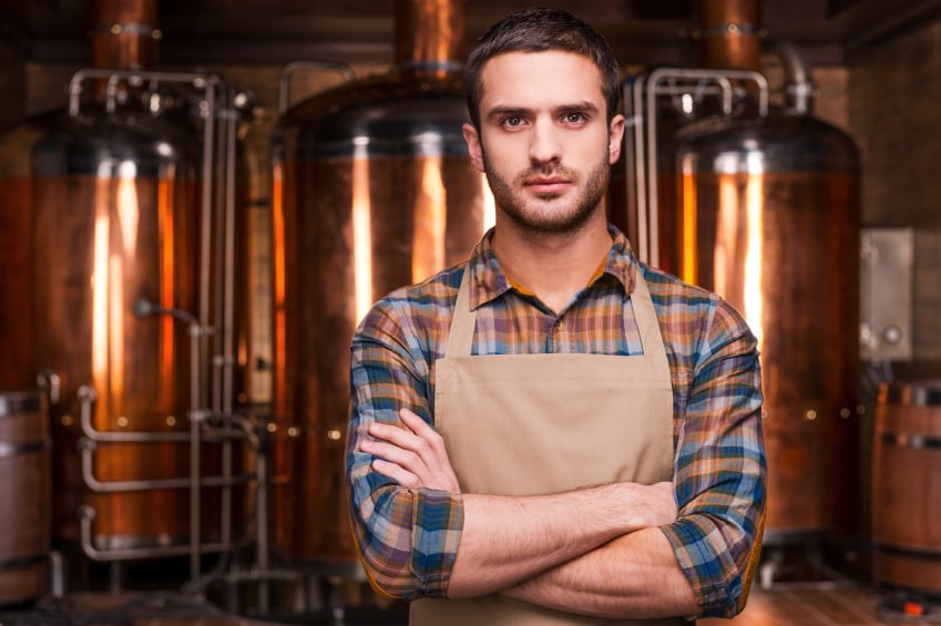 Young brewer in front of metal containers