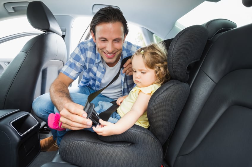 father fastening seatbelt of a baby in car
