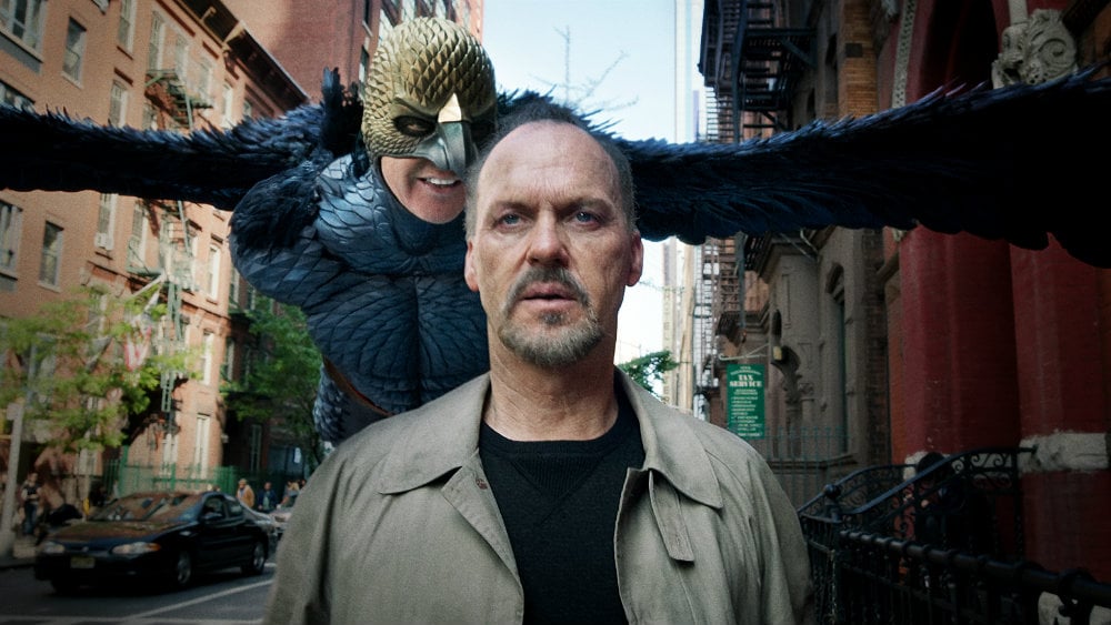 Michael Keaton walking on a city street, as his own character Birdman flies behind him