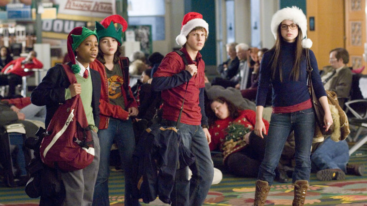 The cast of Unaccompanied Minors are wearing Santa hats and are carrying bags.