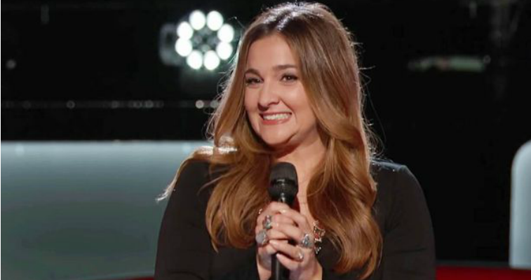 Alisan Porter is smiling and holding a microphone on The Voice.