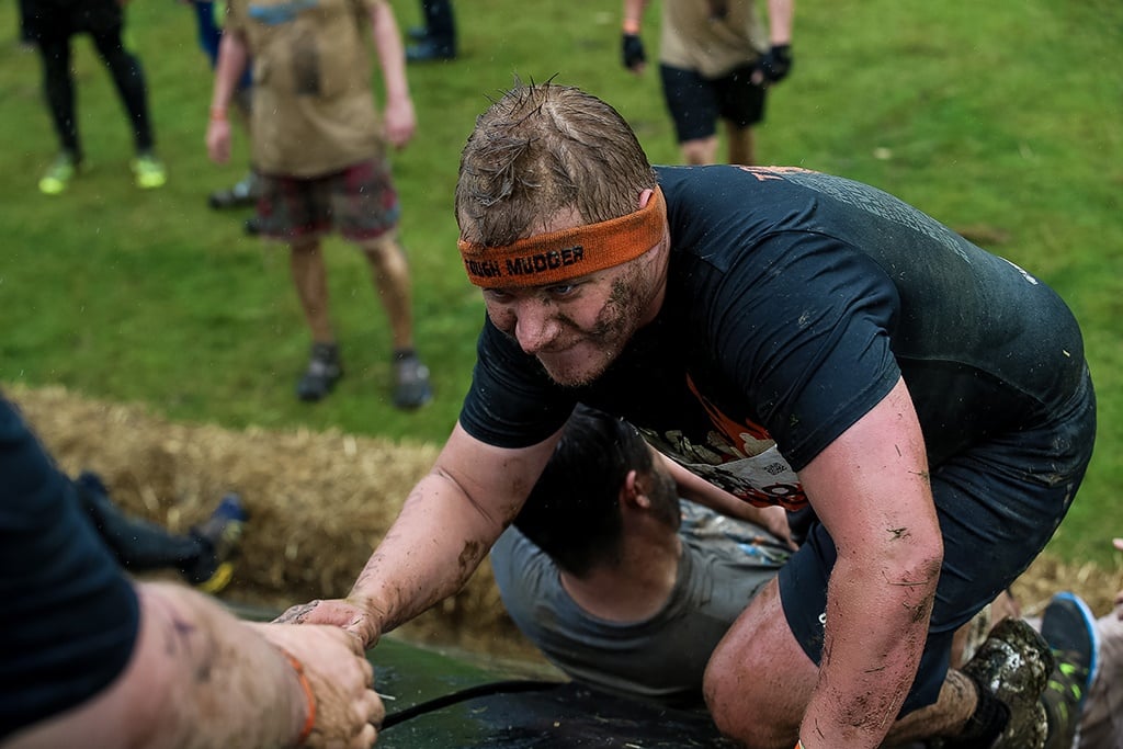 man climbing and obstacle with the hlep of other participants at Tough Mudder