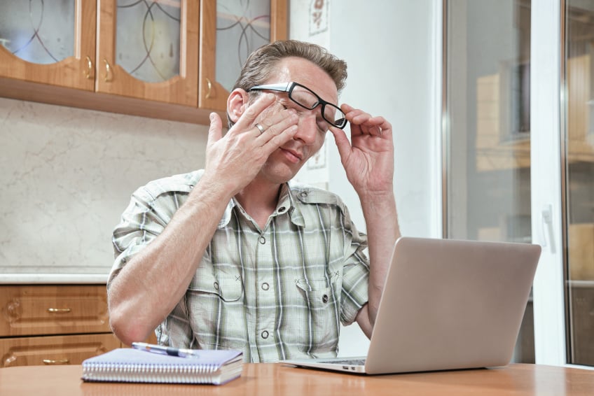 man rubbing his eyes while he works on a laptop