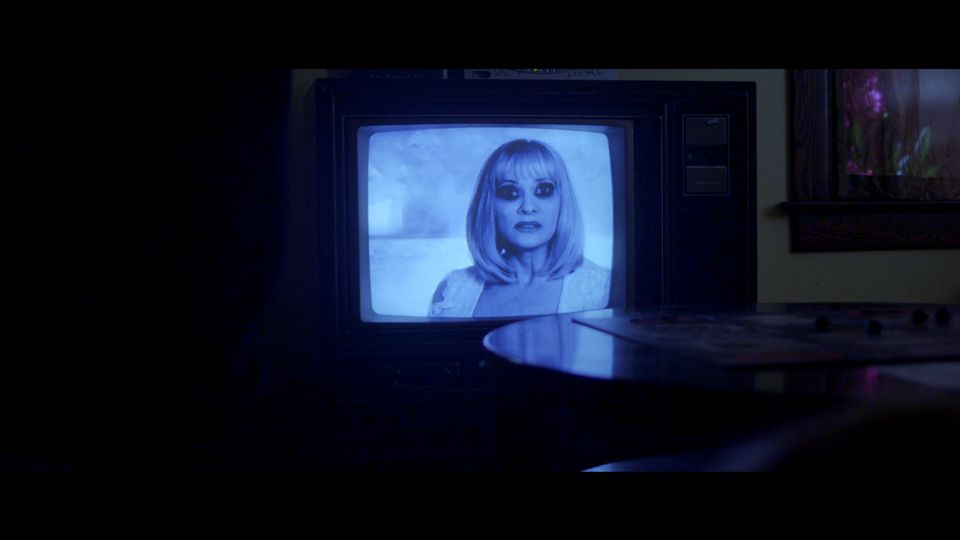 A woman on a TV screen in a dark room in a scene from Beyond the Gates