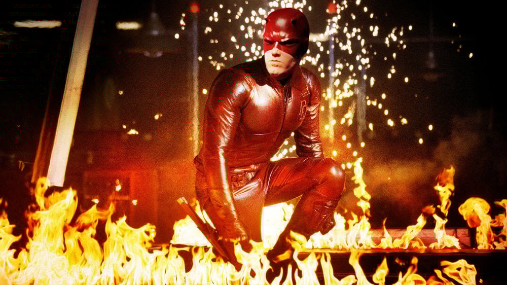 Ben Affleck suited up in a red costume in 'Daredevil' crouching amid flames