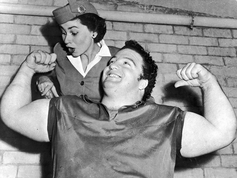 Muscle-bound member of the US Olympic weightlifting team shows off his bulging biceps to an open-mouthed stewardess