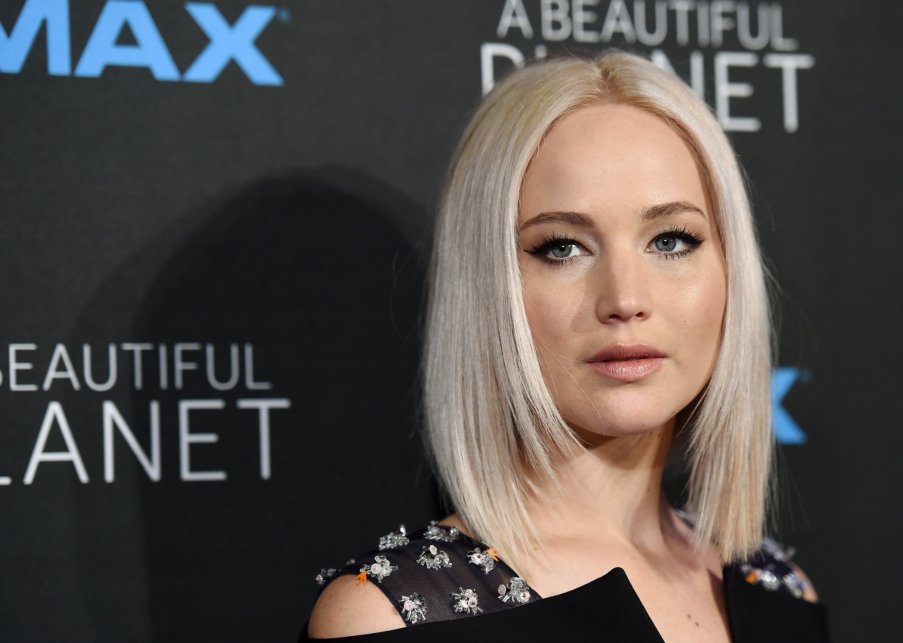 Jennifer Lawrence posing on the red carpet in a black floral dress as she stares straight ahead.