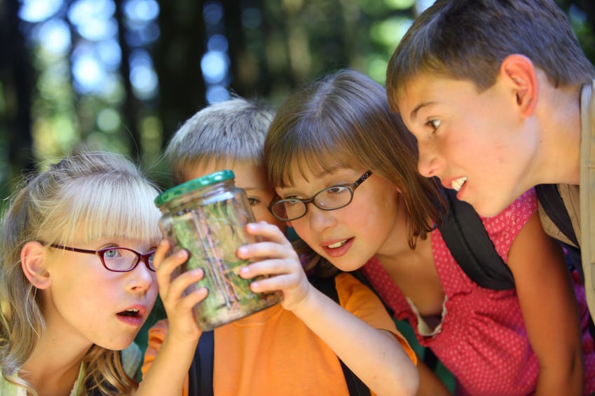 group of children outside looking at a bug they caught in a jar