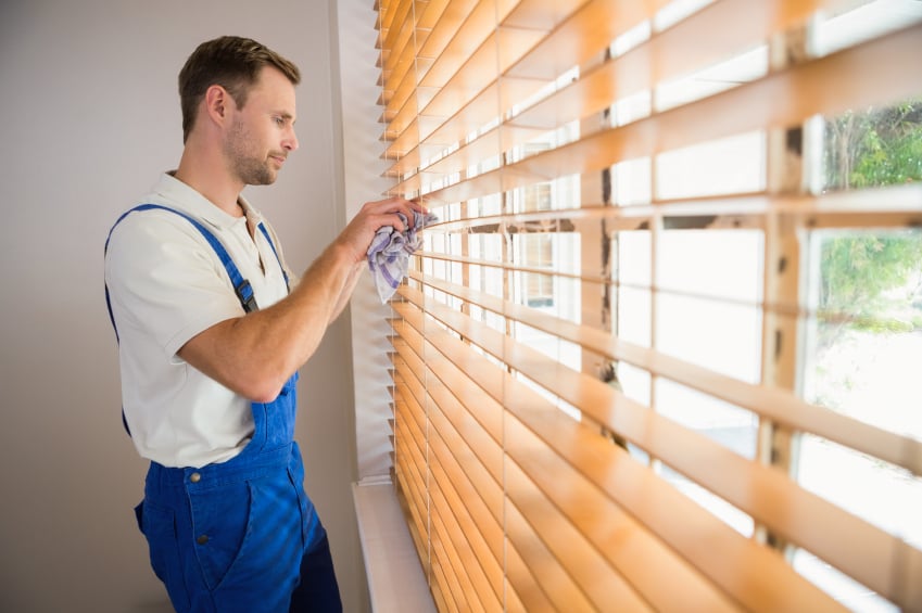 man cleaning blinds with a towel